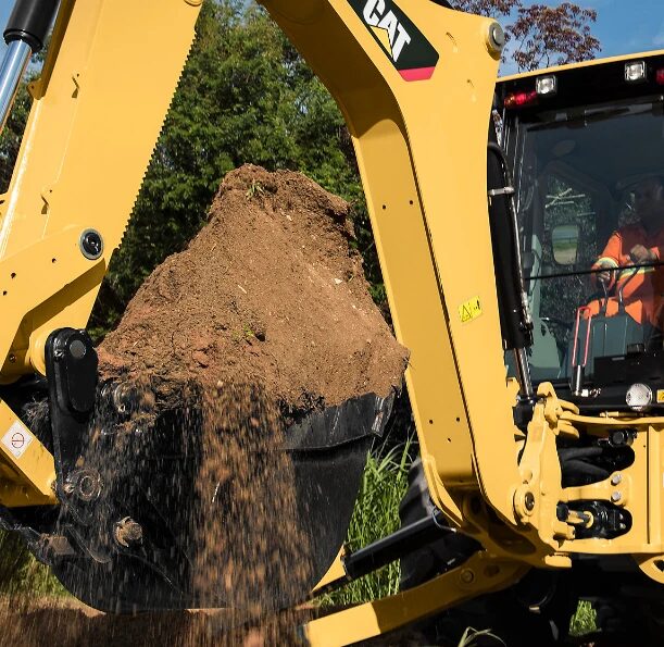 Backhoe bucket lifting a full load of dirt on a job site