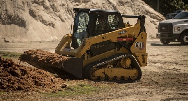 Compact track loader pushing a bucket of dirt across a work site
