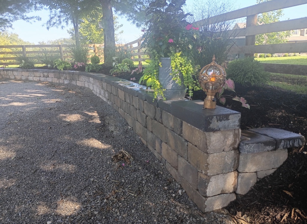 Curved block retaining wall bordering a planted bed and gravel drive