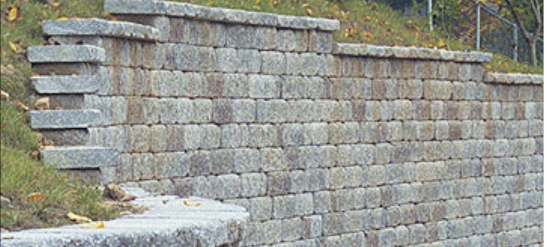 Tiered gray block retaining wall stepping down a grassy slope